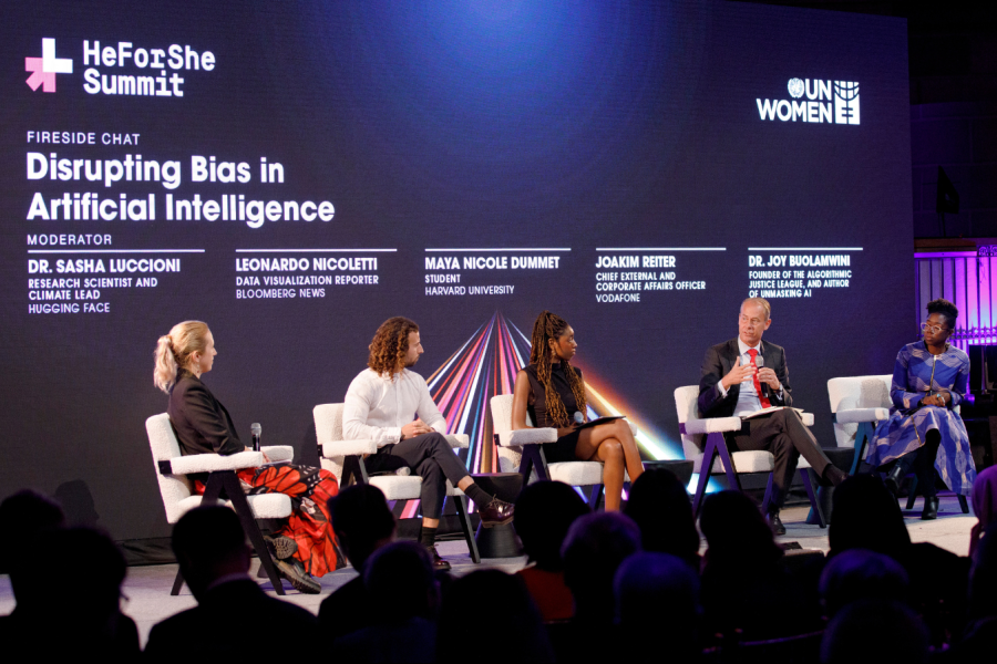 Three women and two men sit on a panel in front of an audience. The screen behind them reads: 'Disrupting Bias in Artificial Intelligence'